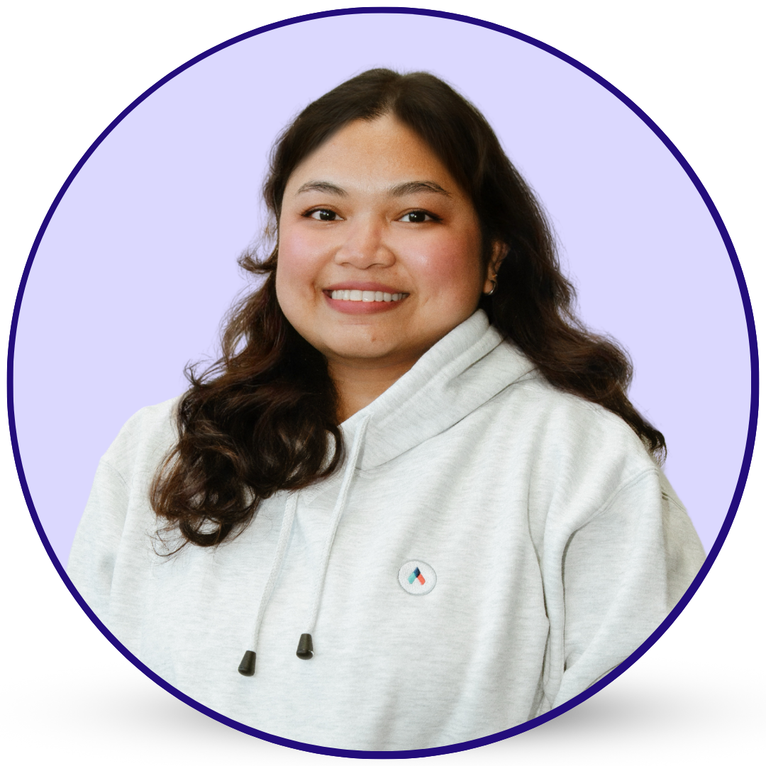 Smiling woman with dark wavy hair in a grey hoodie, framed by a purple circle.