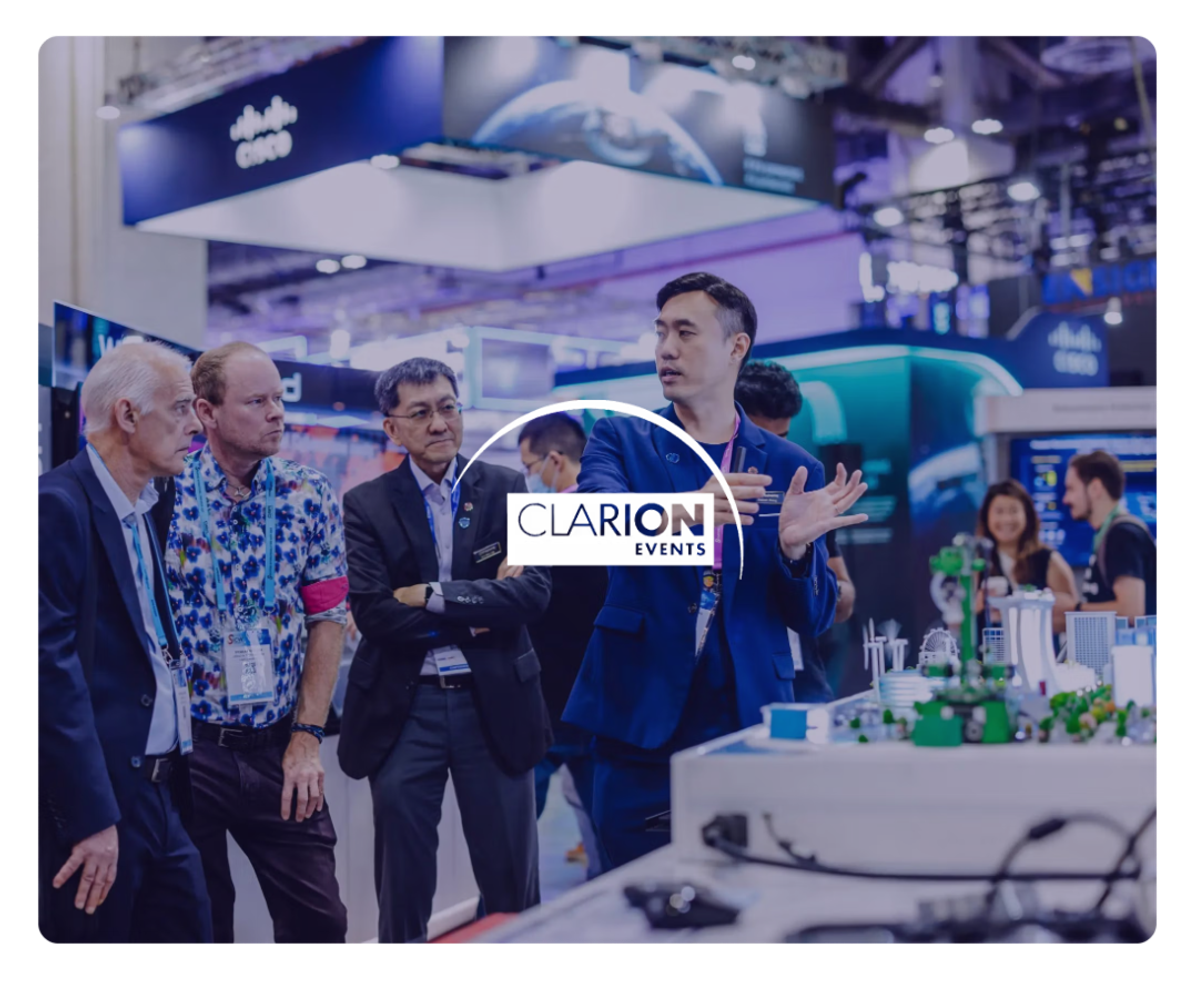 A man presents a model city at a trade show to three other men, with the Clarion Events logo overlaid.