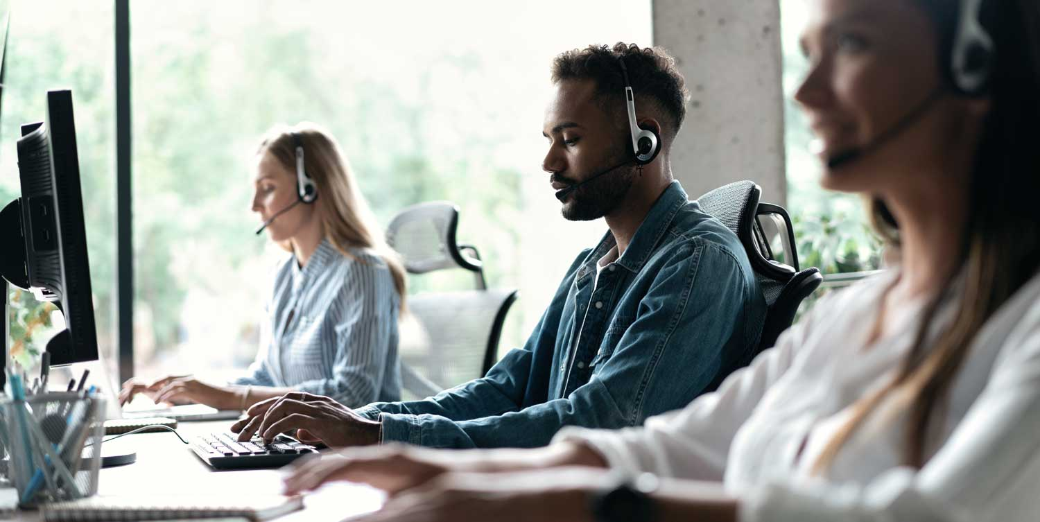 Three call center agents wearing headsets and typing on computers.