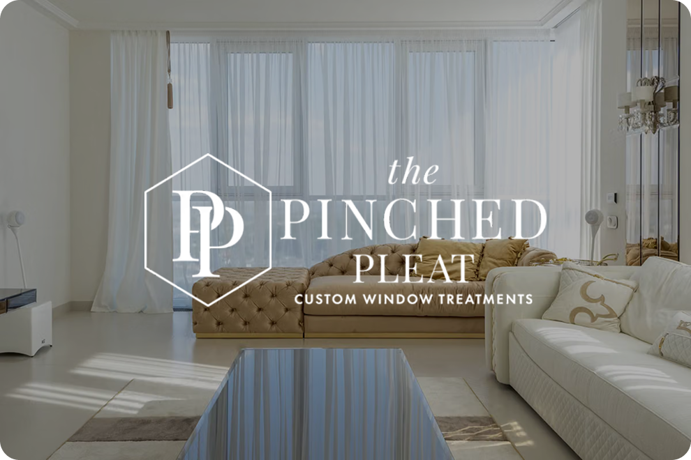 Logo for The Pinched Pleat Custom Window Treatments over a stylish living room with sheer white curtains.