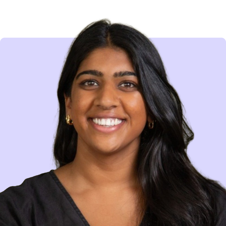 A smiling young woman with dark skin and long dark hair, wearing a dark top.