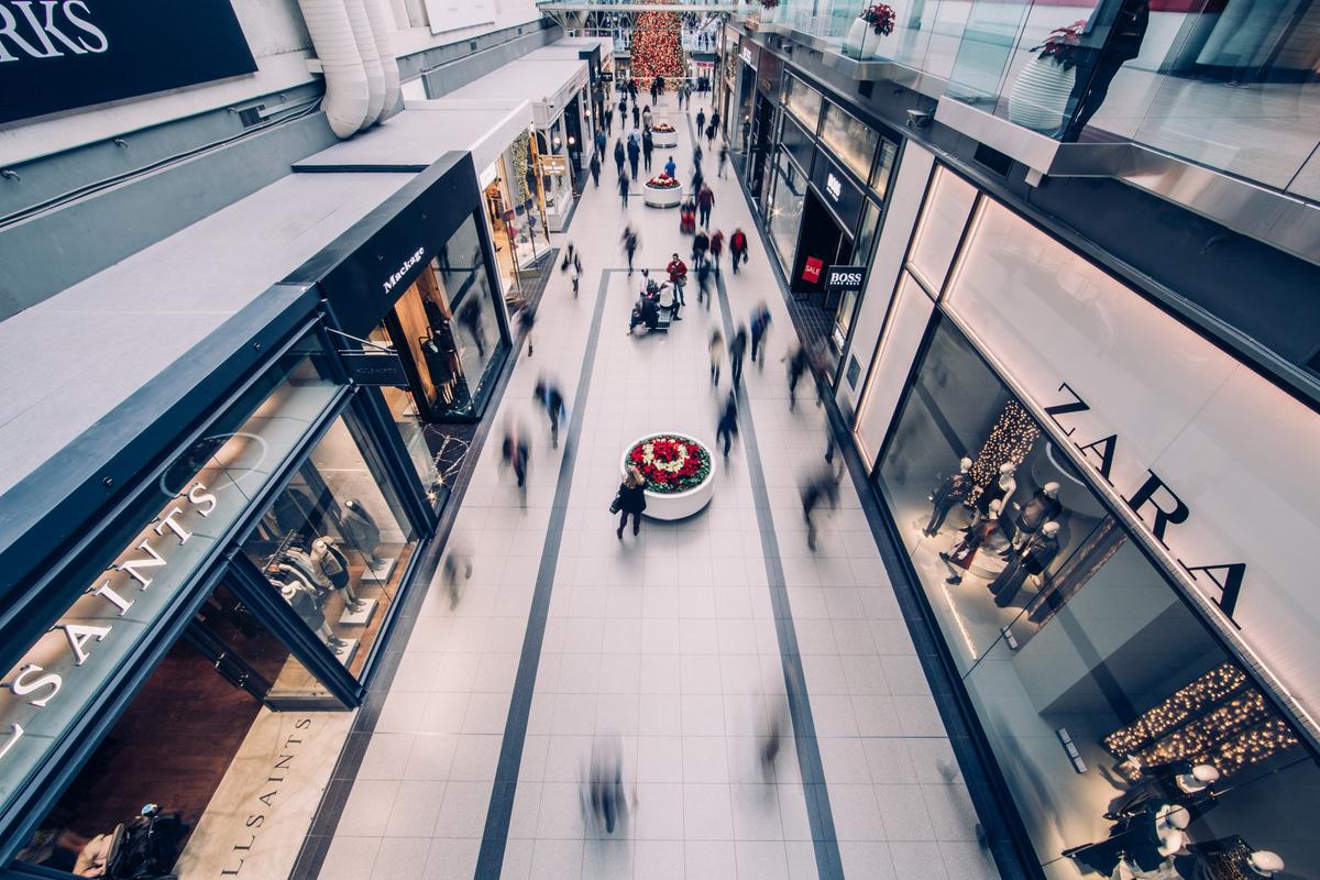 Overhead view of a bustling shopping mall with motion-blurred shoppers and storefronts.