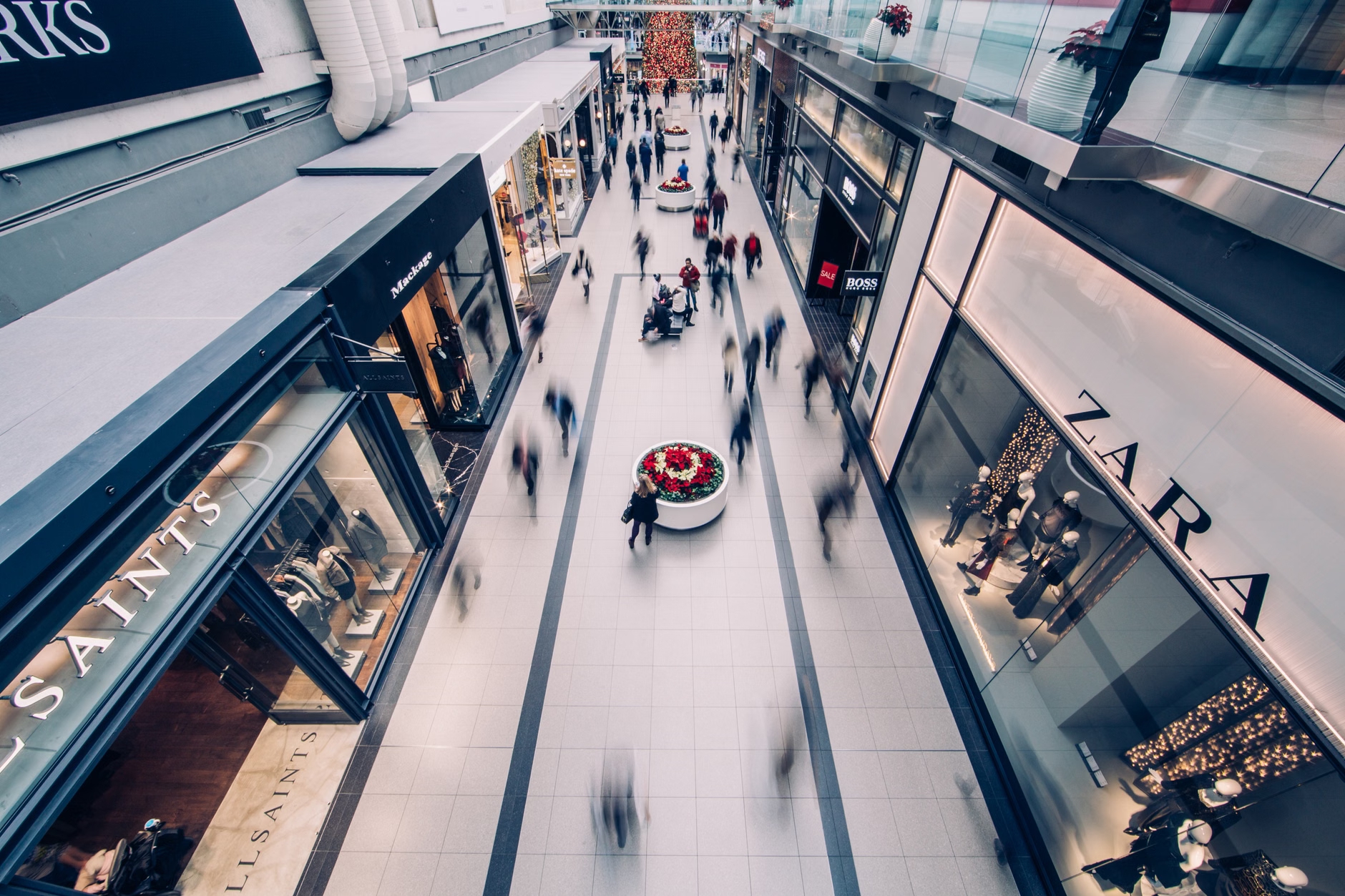 Overhead view of a bustling shopping mall with motion-blurred shoppers and storefronts.