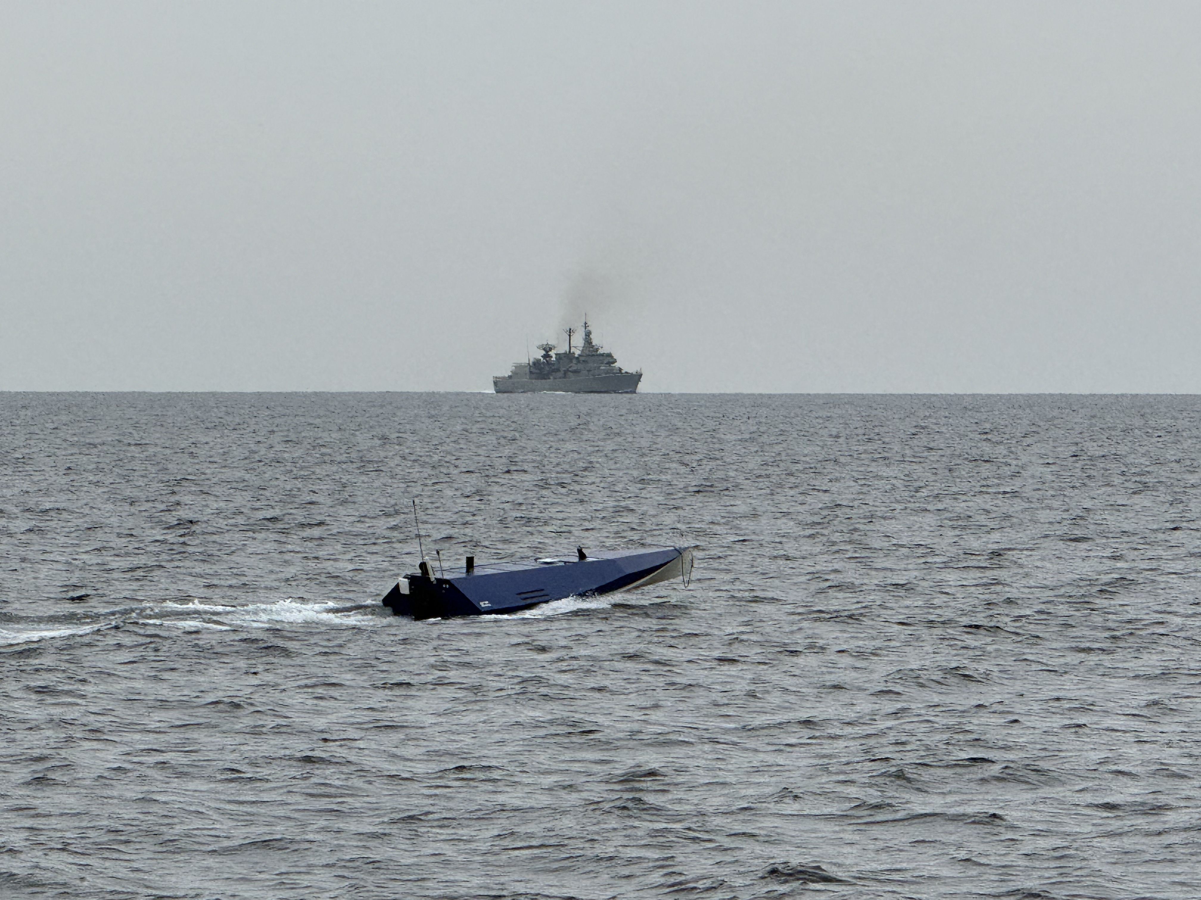 USV running at sea with a naval escort vessel visible on the horizon