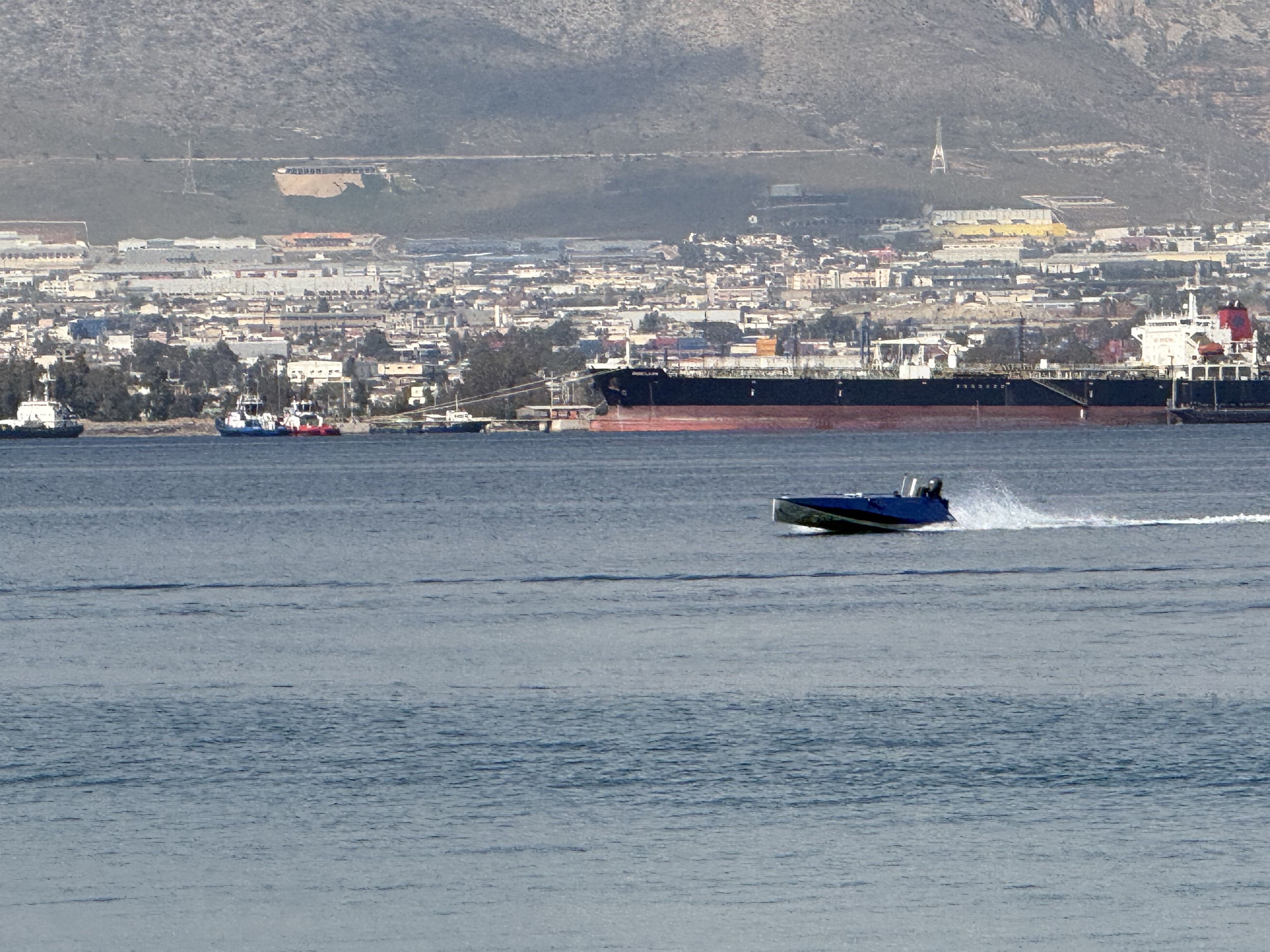ER69D running at speed on open water, Saronic Gulf coastline in the background
