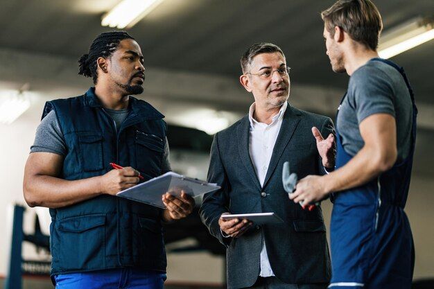 A manager in a suit talks with two mechanics in work vests in a workshop