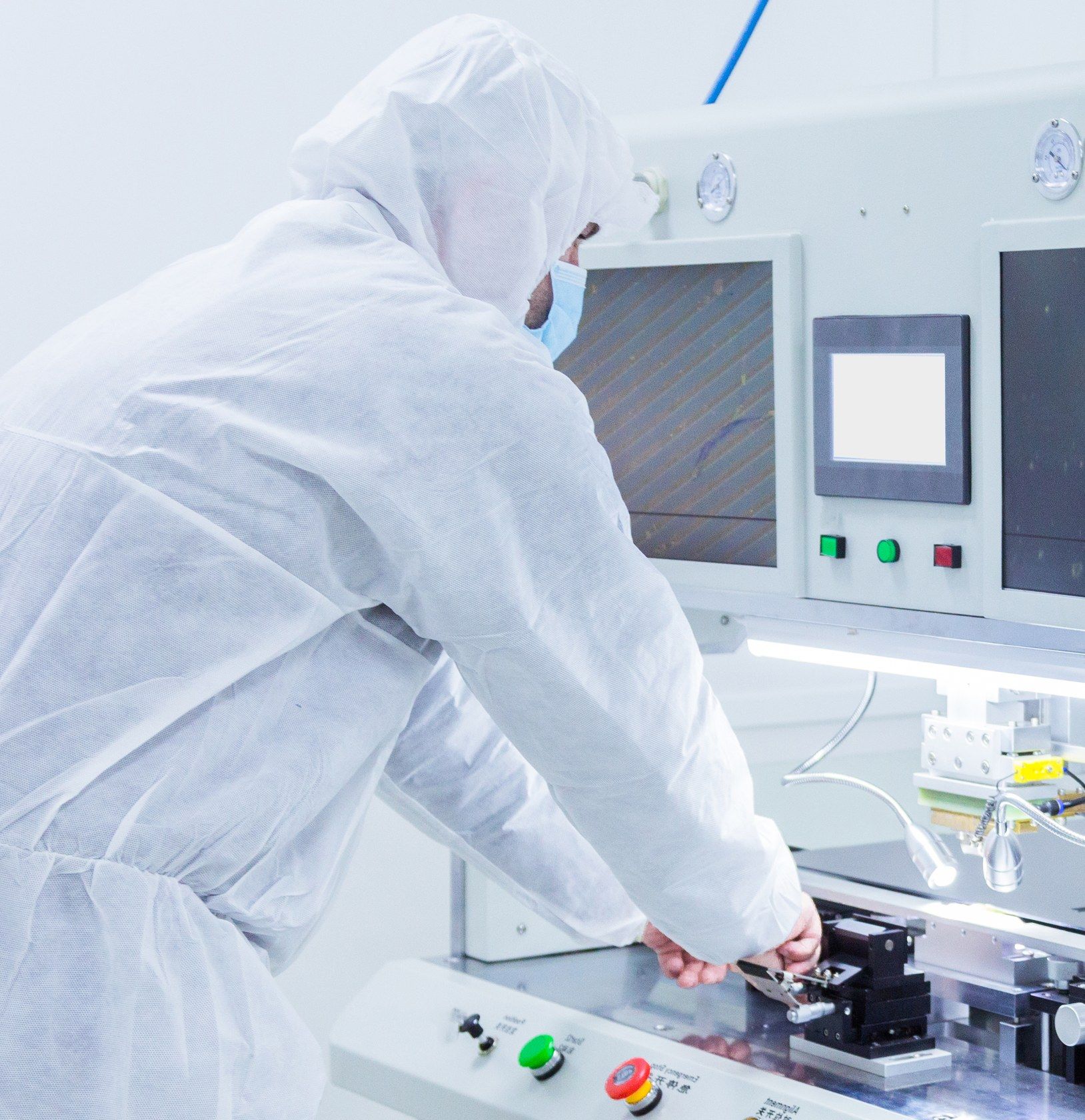 A technician in a white cleanroom suit operates equipment in a medical device lab