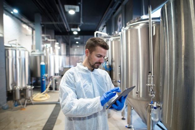 Worker with a tablet inspecting stainless steel tanks in a food plant