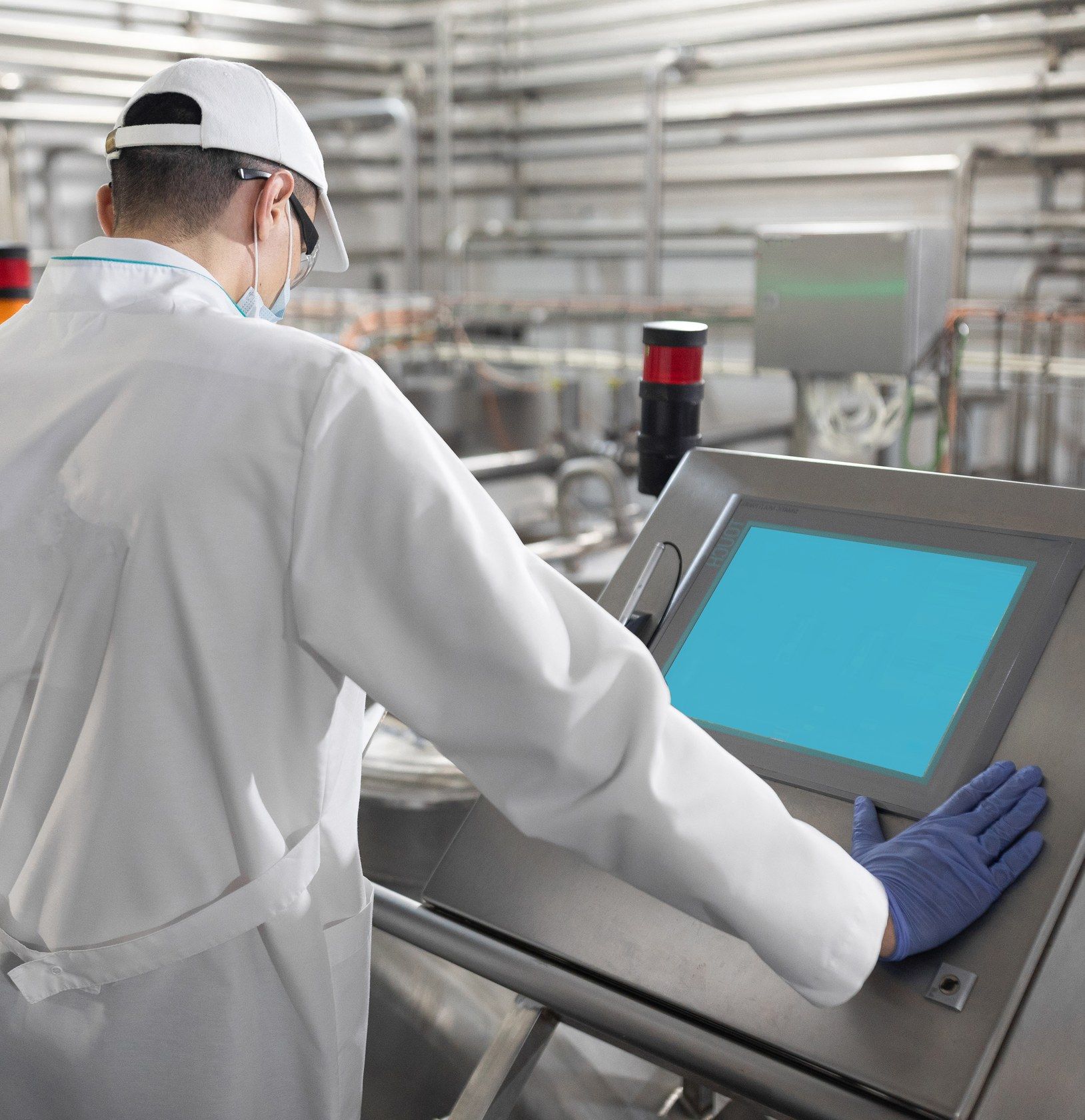 Un opérateur en blouse, casquette et gants utilise un écran de commande dans une usine agroalimentaire