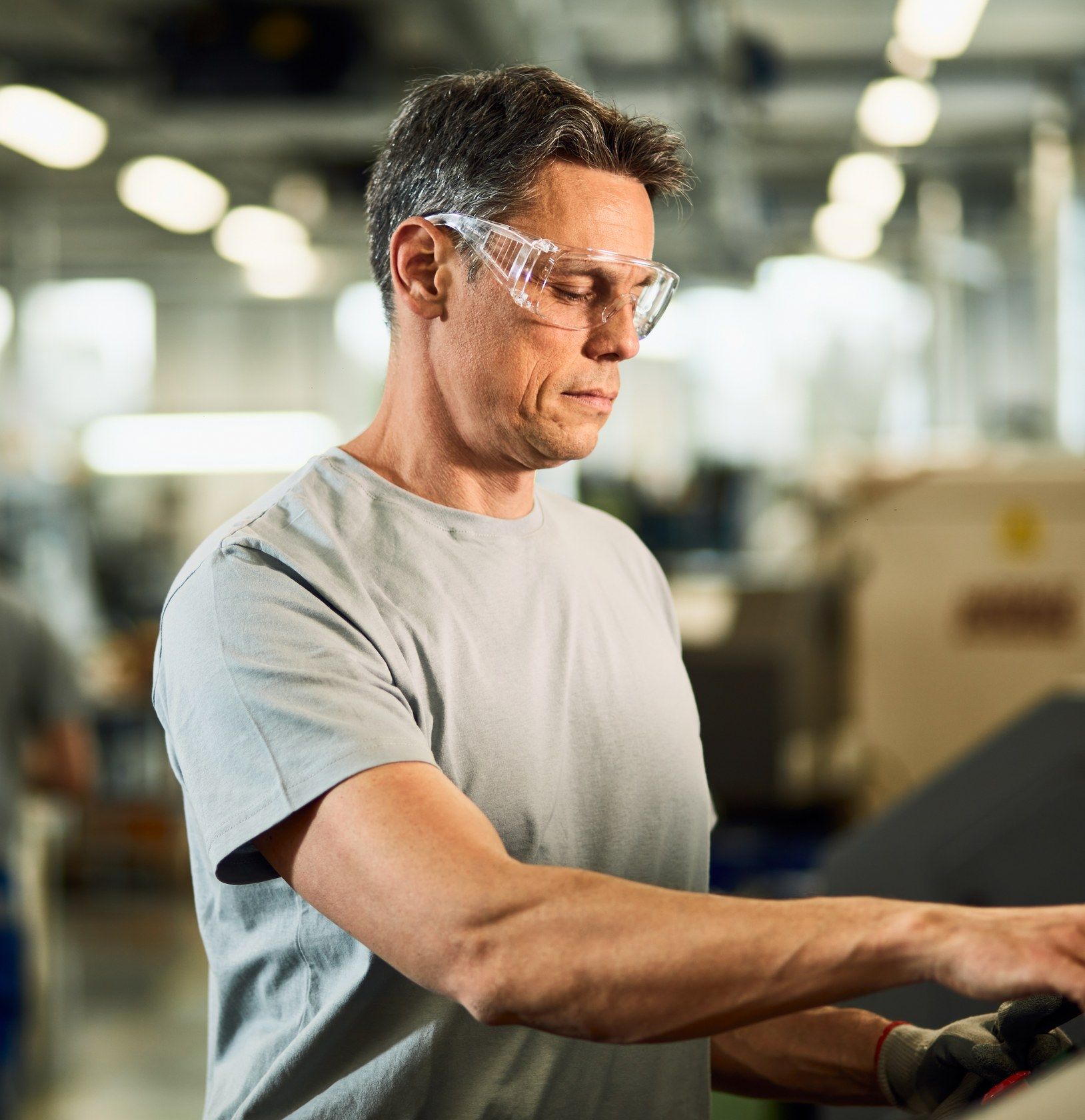 An operator wearing safety glasses works at a machine on the factory floor