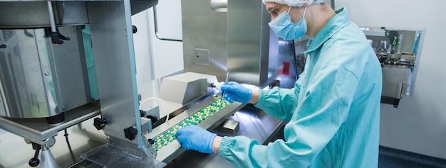 Lab technician in protective clothing working at a pharmaceutical production line