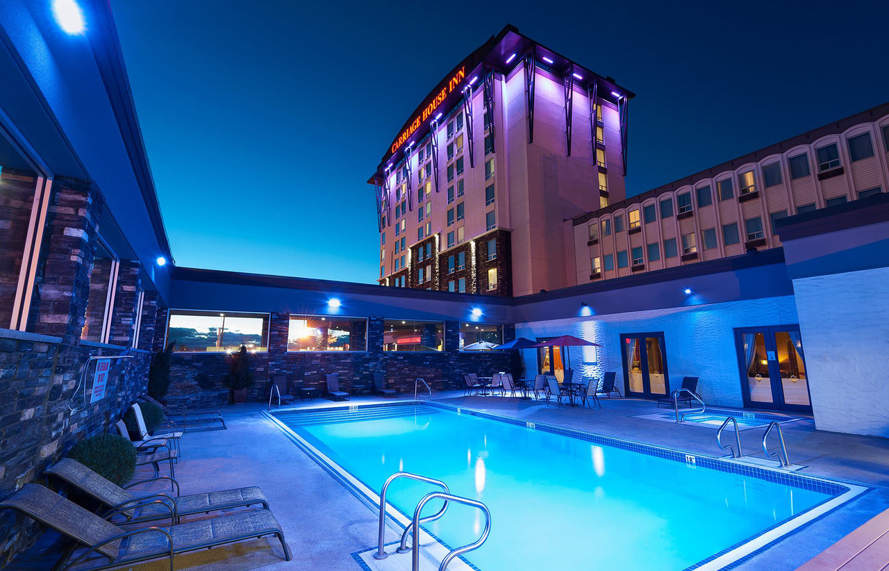 The exterior of Carriage House Hotel at night, with a focus on the patio and outdoor pool, which is surrounded by lounge chairs.