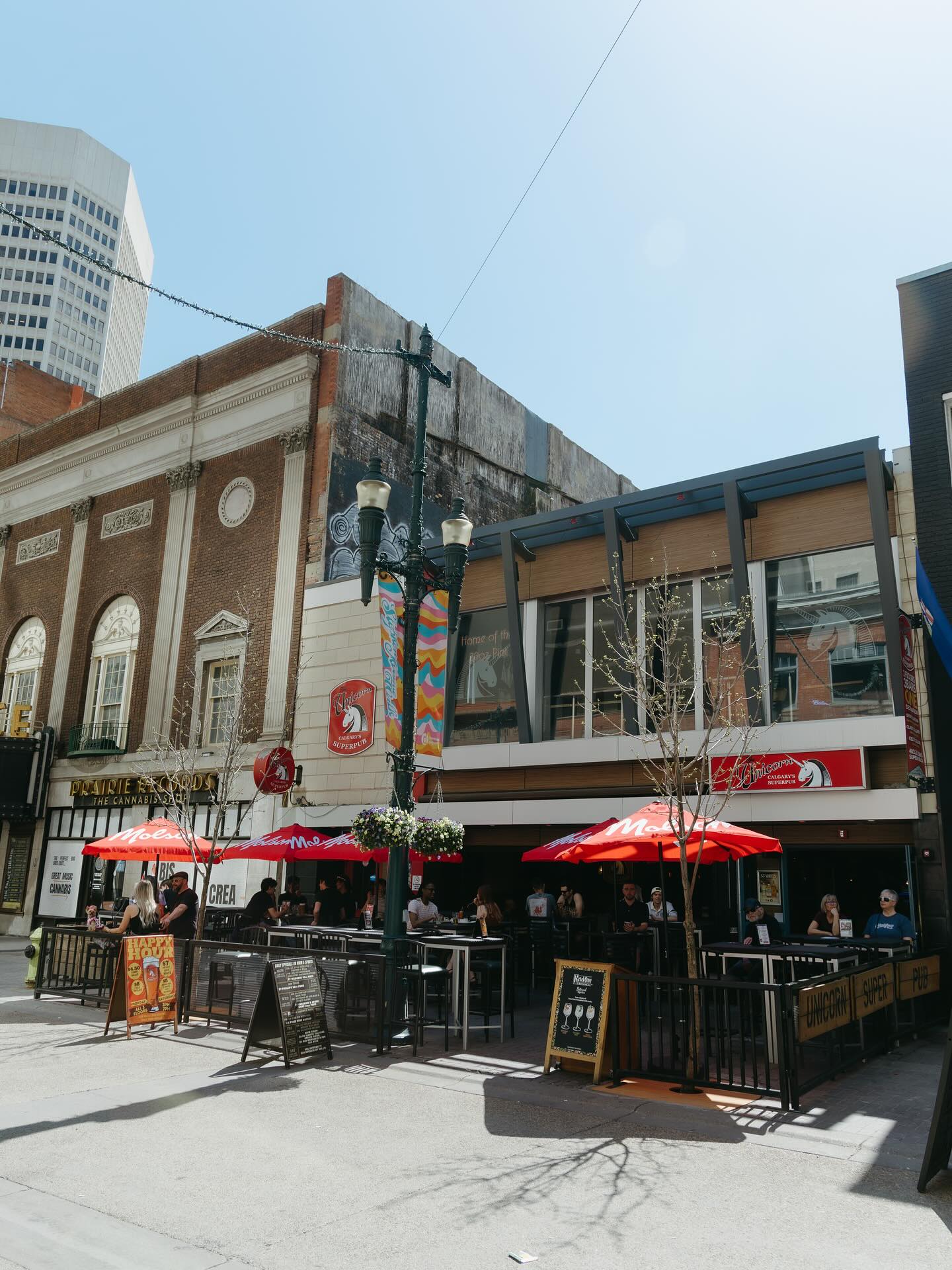 Exterior of Unicorn Pub’s multistorey location in downtown Calgary. The street-level patio is filled with customers.