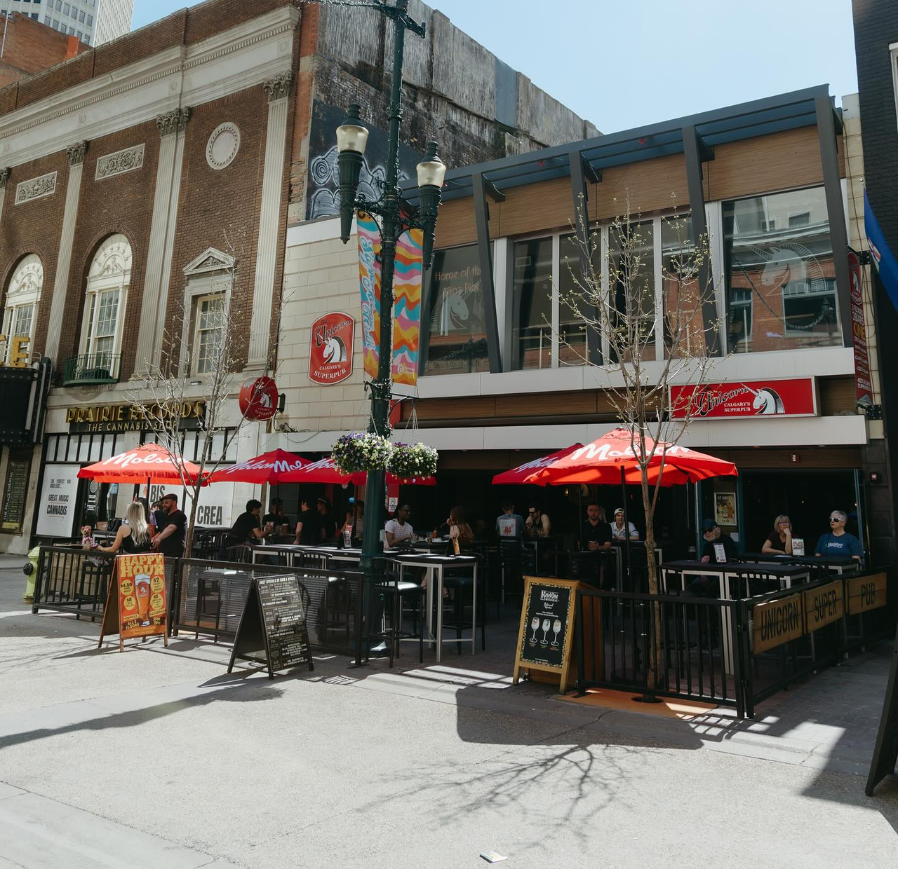 Exterior of Unicorn Pub’s multistorey location in downtown Calgary. The street-level patio is filled with customers.