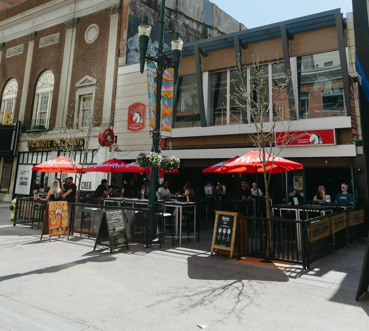 Exterior of Unicorn Pub’s multistorey location in downtown Calgary. The street-level patio is filled with customers.