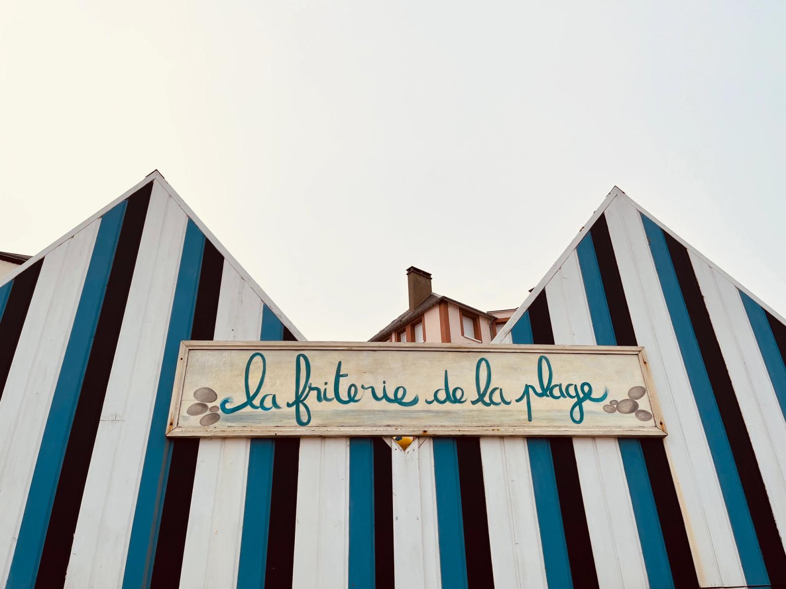 wooden houses painted lightblue, darkblue and white, with a sign that says la friterie de la plage