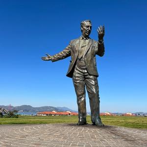 statue of man who seems to give a speech in front of ocean with blue sky and surrounded by grass