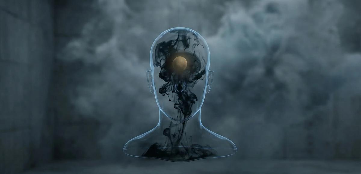 Uma escultura de vidro transparente em forma de cabeça e ombros está suspensa por um fio fino no centro de uma sala de concreto sombria. Dentro da escultura, uma esfera dourada e brilhante no lugar do cérebro é envolvida por uma nuvem de tinta preta e ondulante que se espalha para baixo, obscurecendo parcialmente a luz. A fumaça e o nevoeiro preenchem o fundo cinza e texturizado, criando uma atmosfera misteriosa e etérea. A iluminação é dramática, destacando a esfera dourada e a tinta escura dentro da forma vítrea.