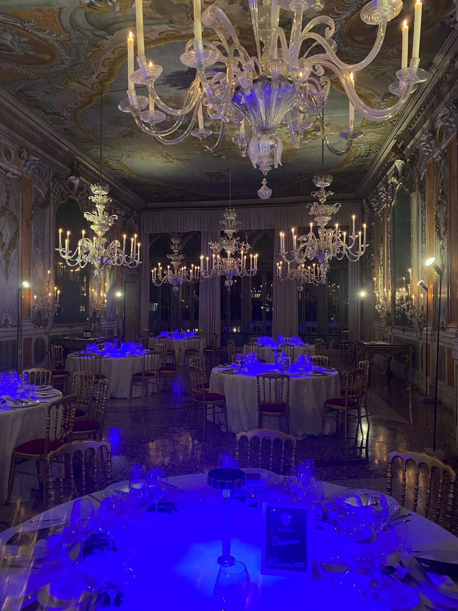 sala di un palazzo veneziano con tavoli apparecchiati illuminati da luci blu