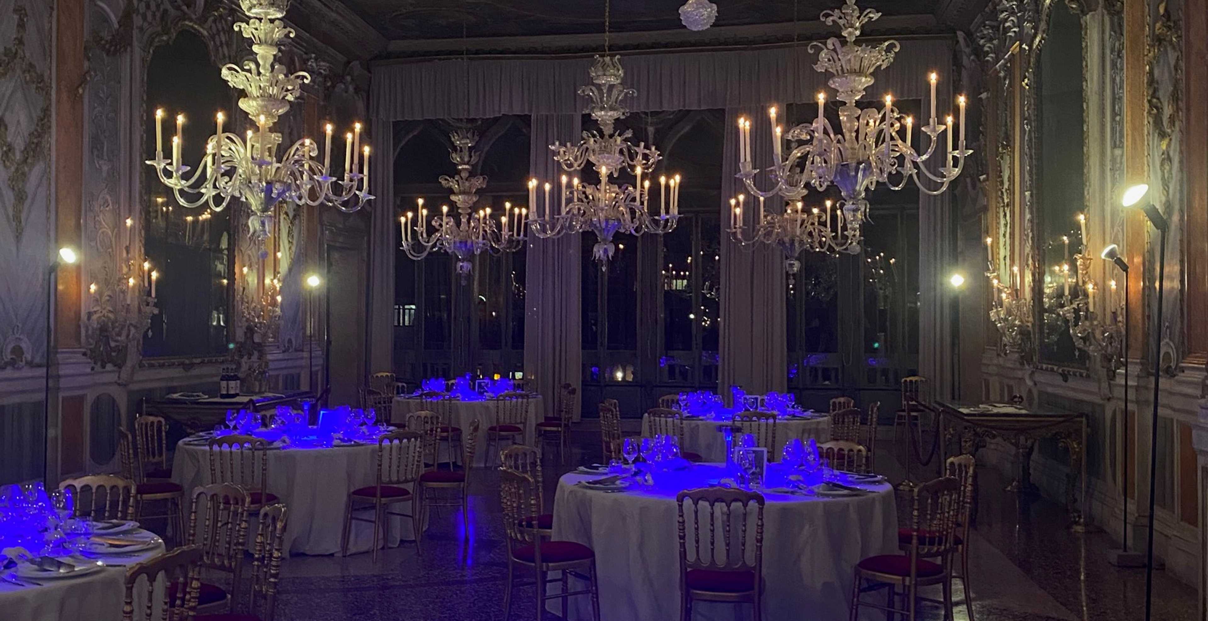 sala di un palazzo veneziano con tavoli apparecchiati illuminati da luci blu