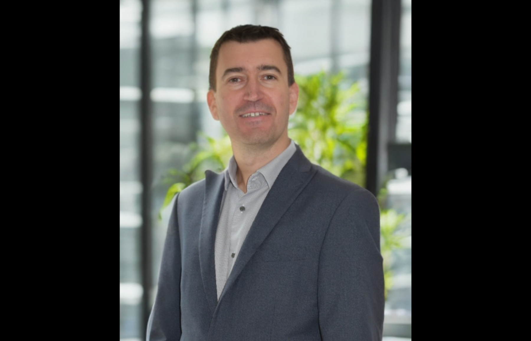 Philip Wray, VivoPower Group Finance Director, in a grey blazer in front of office windows and plants