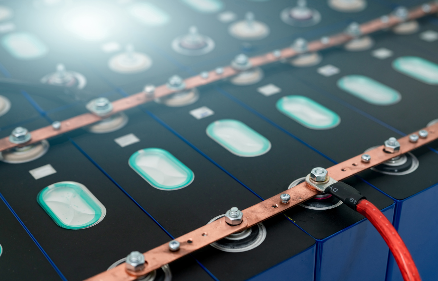 Close-up of prismatic battery cells linked by copper busbars, with a red cable on one terminal