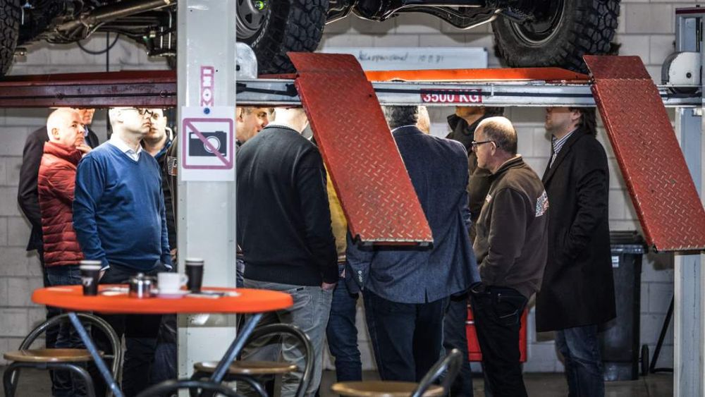 Visitors in conversation beneath a raised vehicle on a workshop hoist at the Tembo 4x4 e-LV unveiling