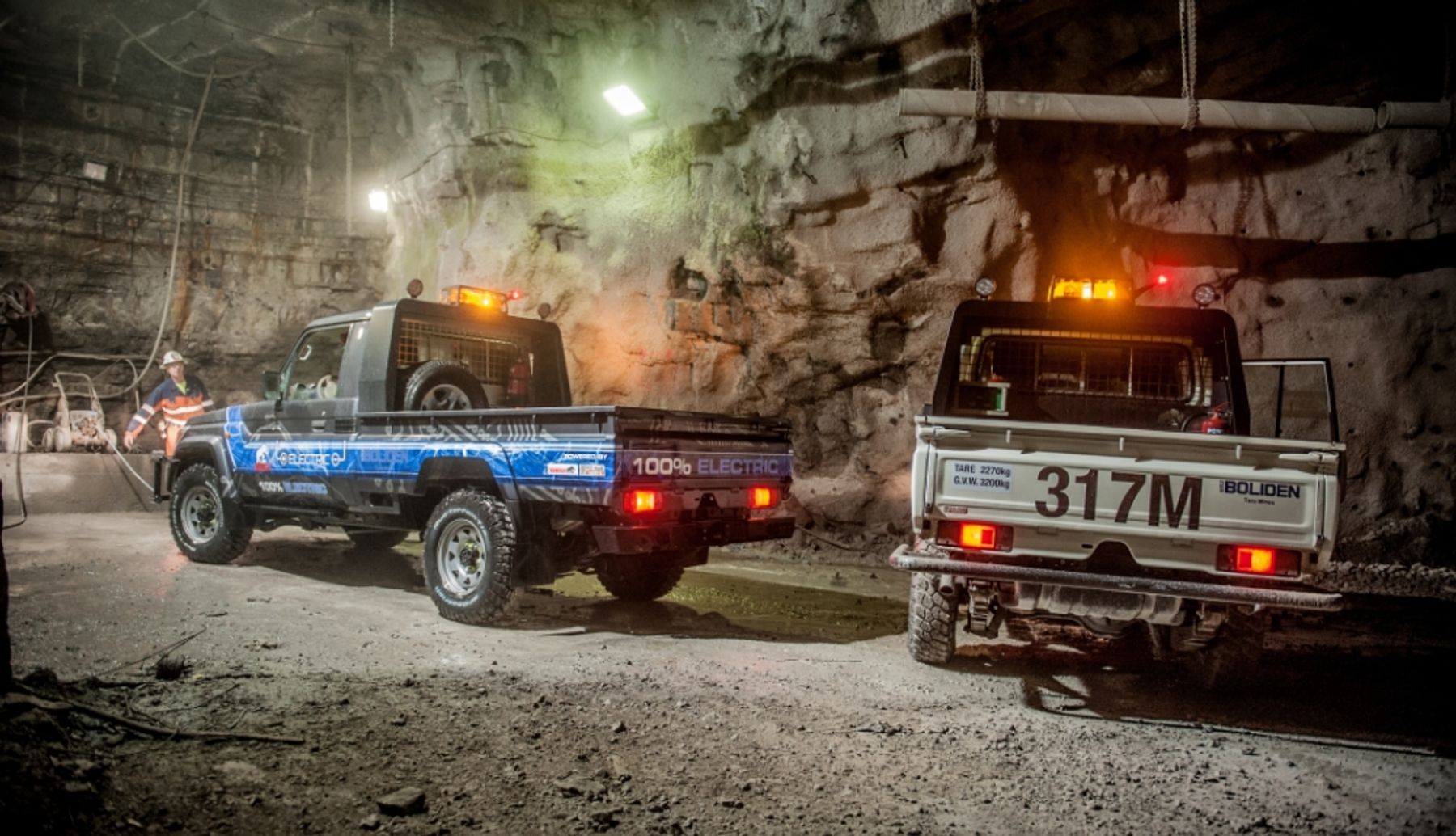 Two electric Land Cruiser 70 utes, one with Boliden branding, in an underground mine tunnel with a worker in hi-vis