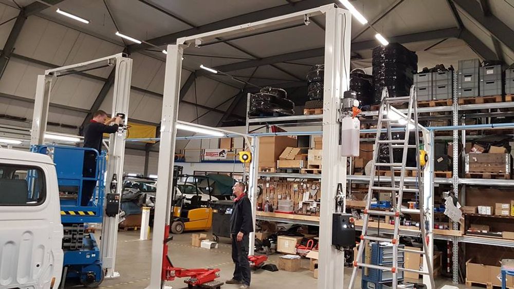 Two technicians installing new two-post vehicle lifts in the Tembo workshop beside shelving stacked with parts