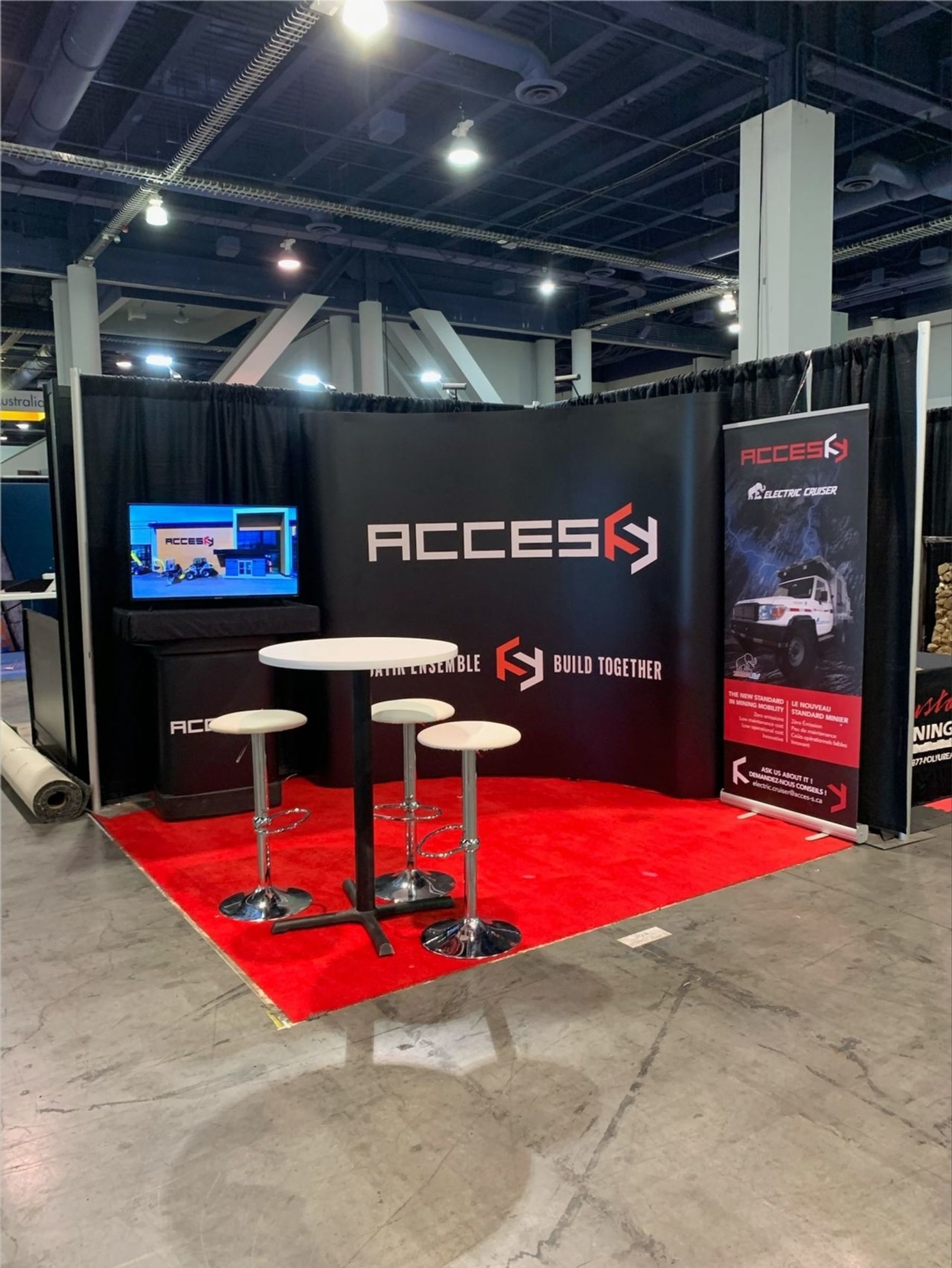Accès exhibition stand at Minexpo with bar stools, a video screen and a banner promoting the electric Land Cruiser