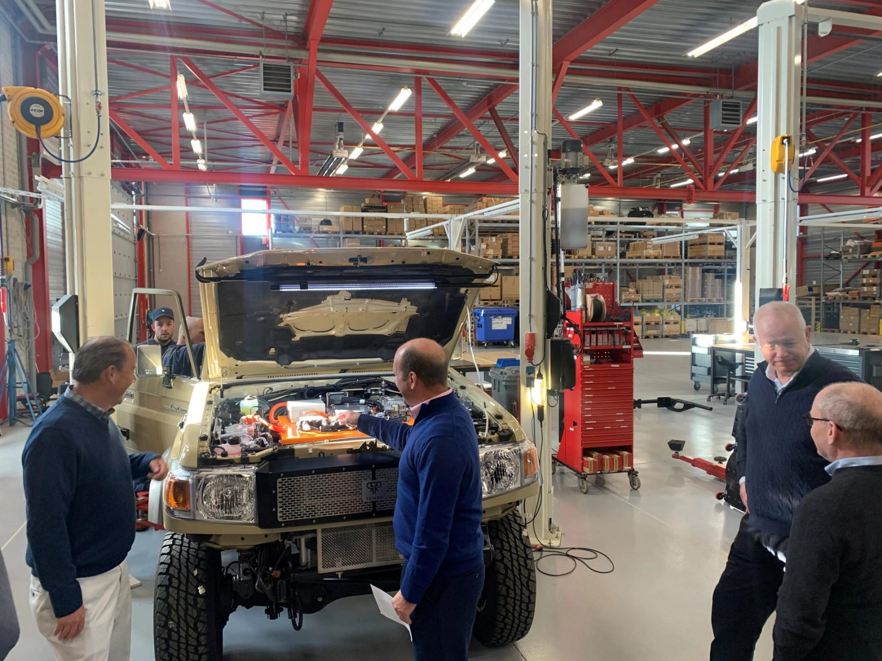 Visitors gathered around an electric Land Cruiser 70 with its bonnet open, showing the electric drive components