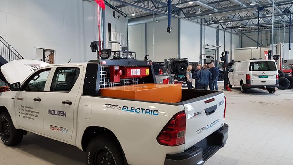 Boliden-branded Tembo 4x4 e-LV Hilux marked 100% electric on display in a workshop, with visitors behind