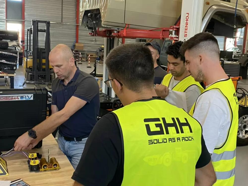 Tembo technician demonstrating electrical components on a workbench to GHH trainees in hi-vis vests
