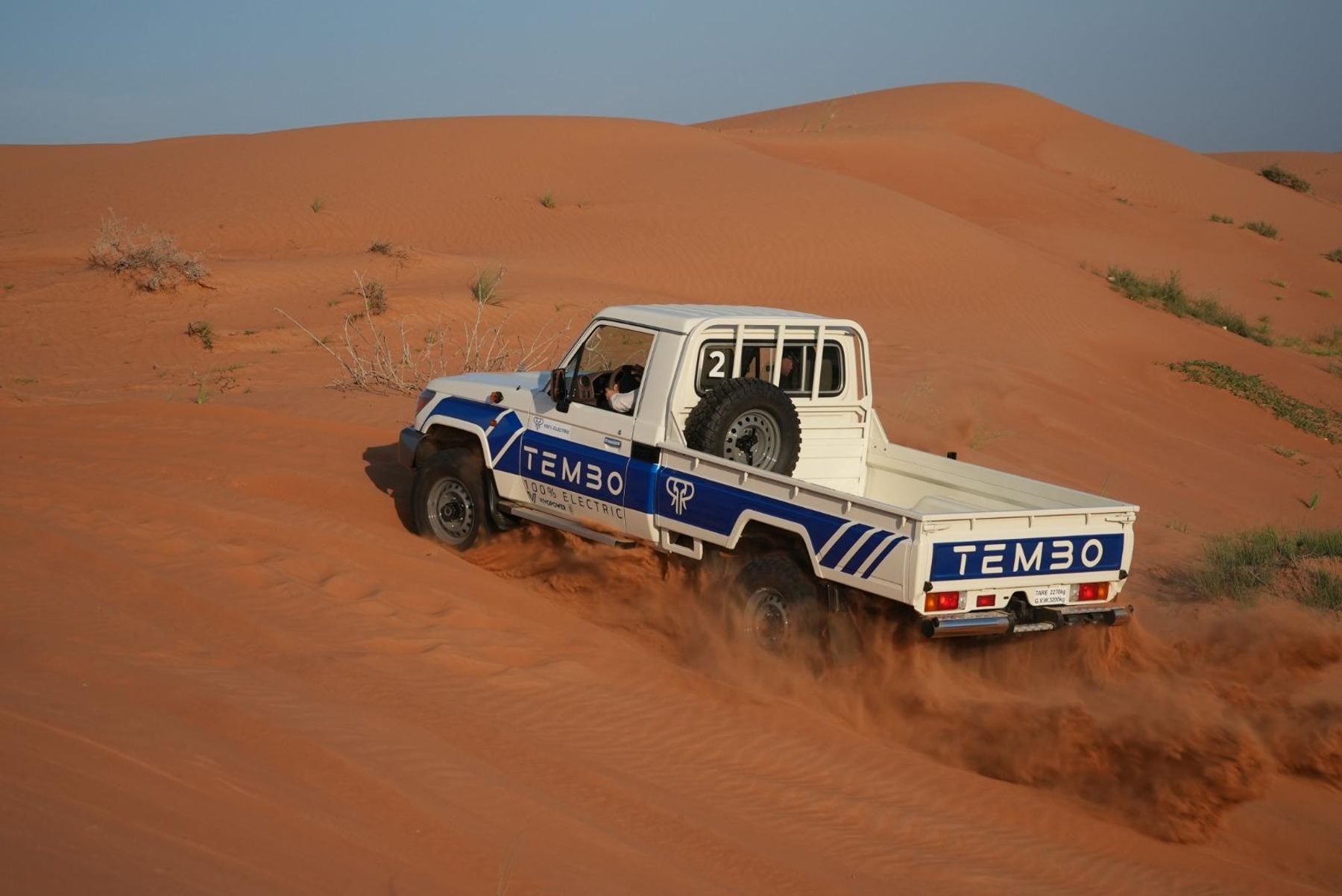 Tembo electric Toyota Land Cruiser 70 series single-cab ute driving through red desert sand dunes