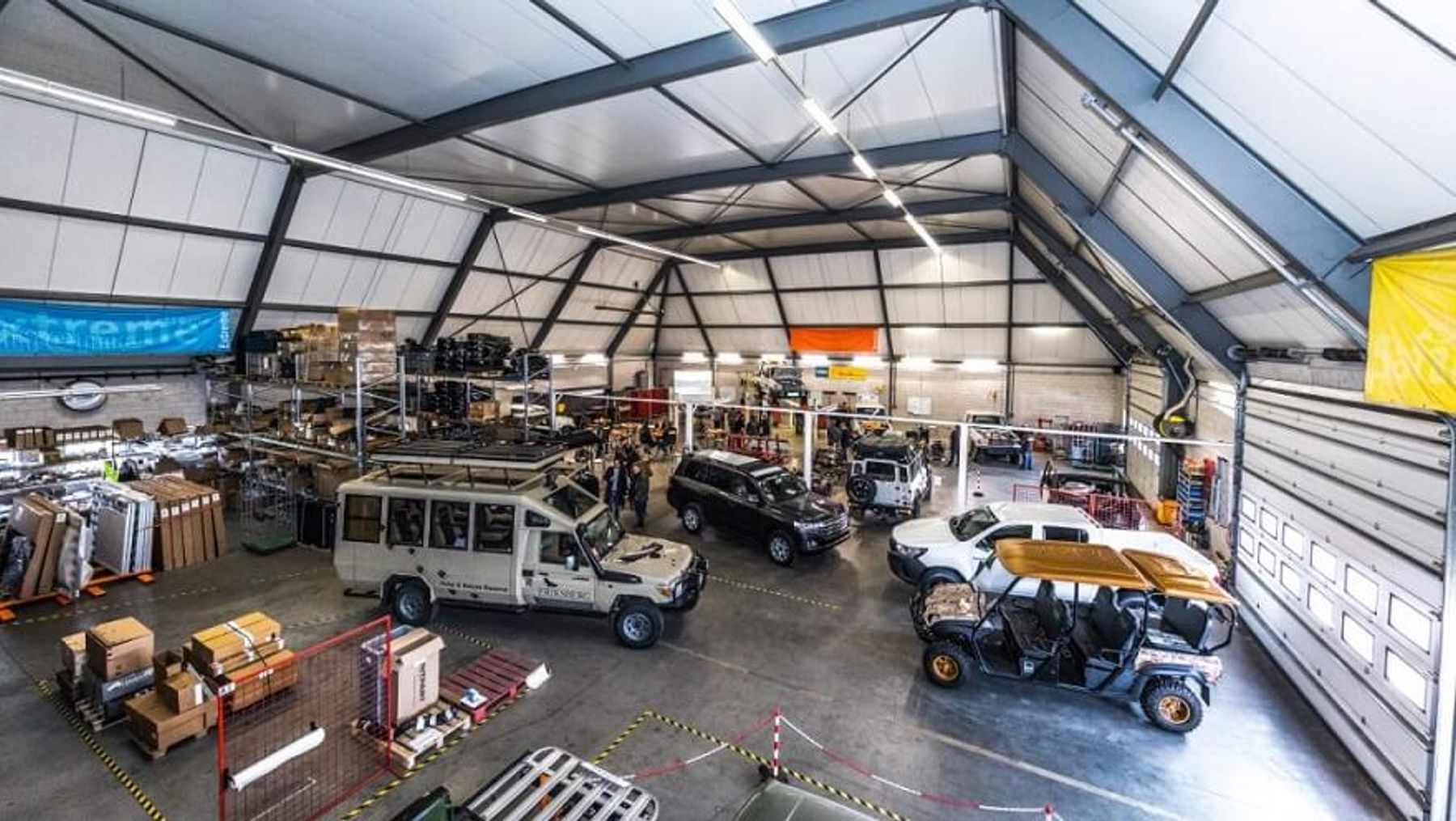 Overhead view of a large workshop with a safari Land Cruiser, utes and an open-sided buggy among parts and pallets