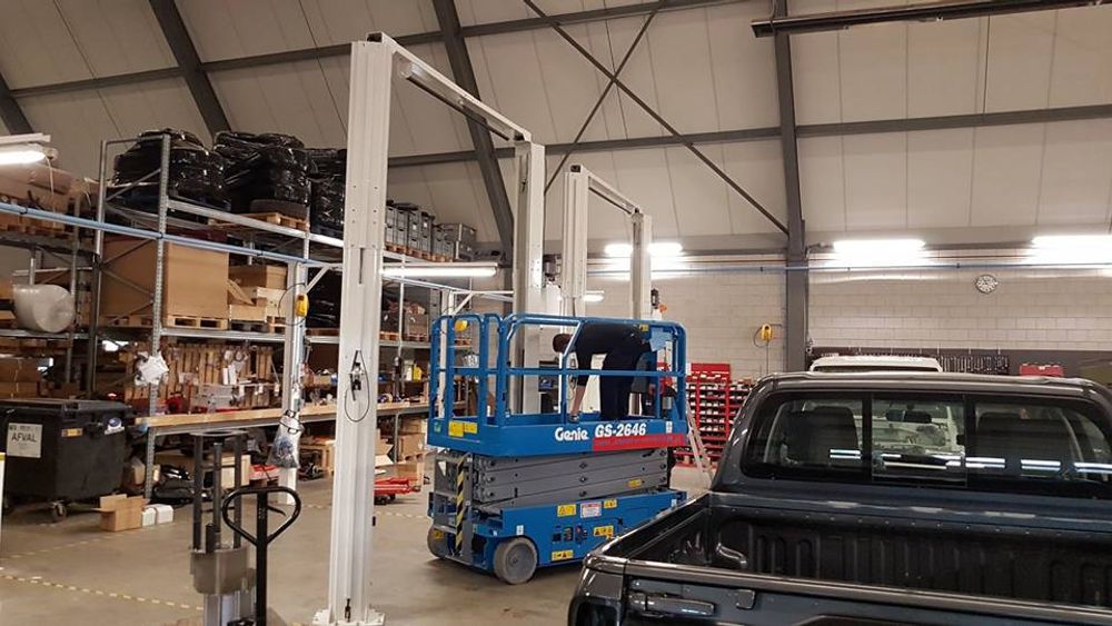 Technician on a scissor lift installing a new two-post vehicle lift in the Tembo workshop, with a ute in the foreground