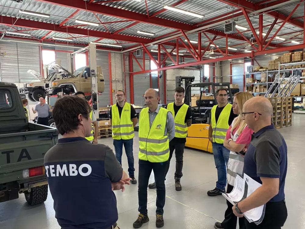 Tembo staff briefing GHH trainees in hi-vis vests in a workshop, with a Land Cruiser raised on a vehicle lift behind