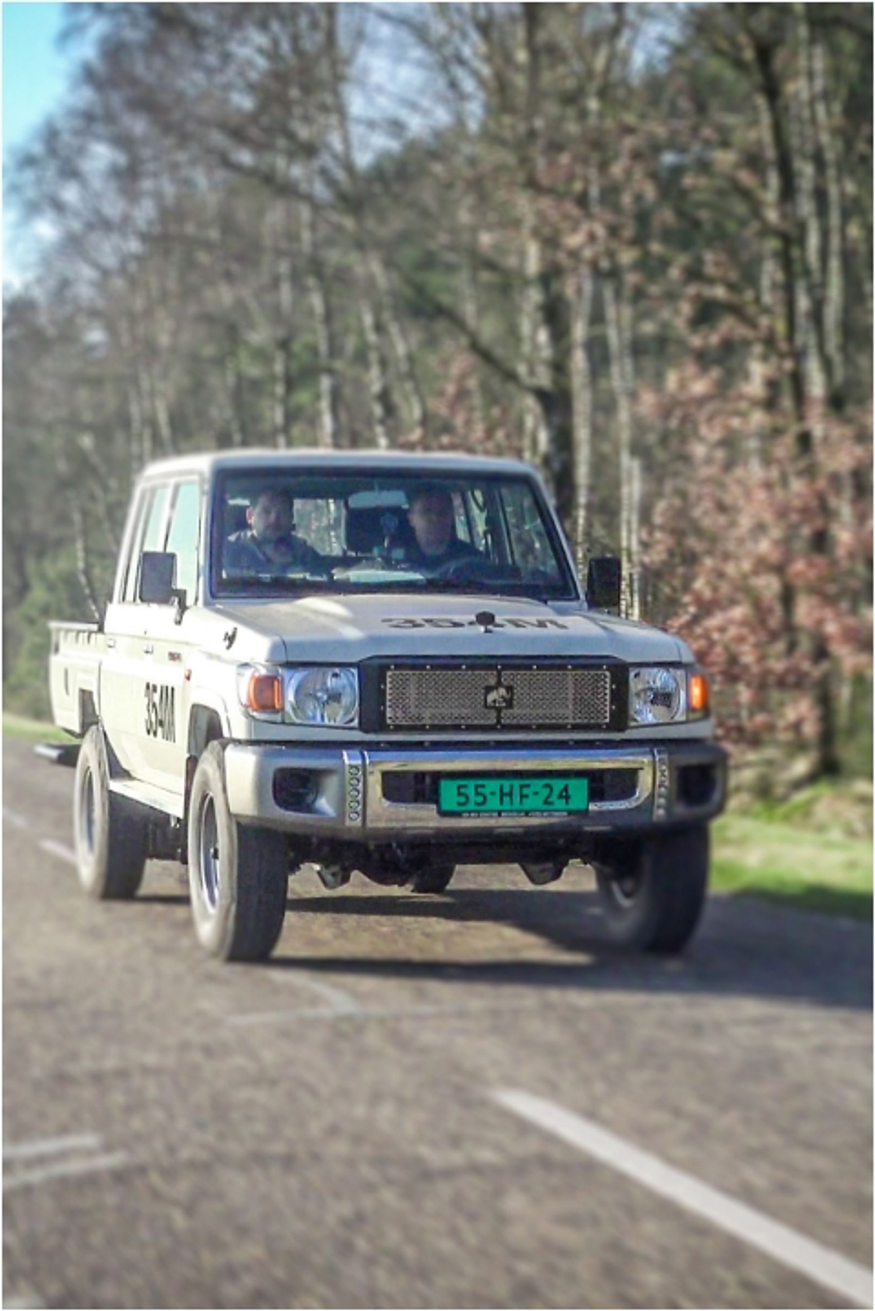 White Tembo electric Land Cruiser 70 series dual-cab ute driving along a tree-lined road