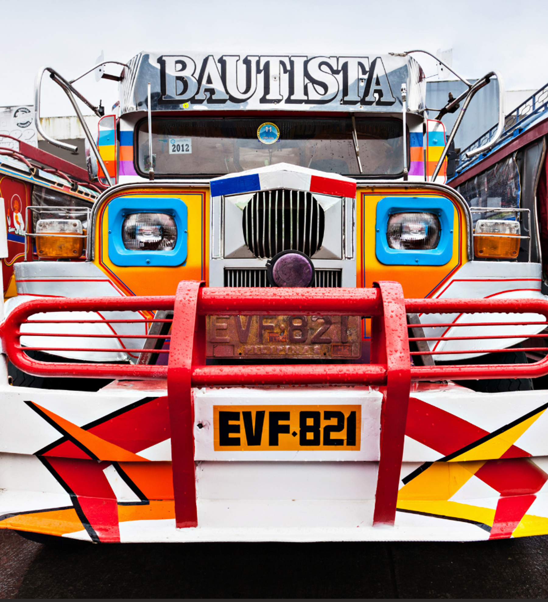 Front of a colourful traditional jeepney with a chrome grille, round headlights and a red bull bar