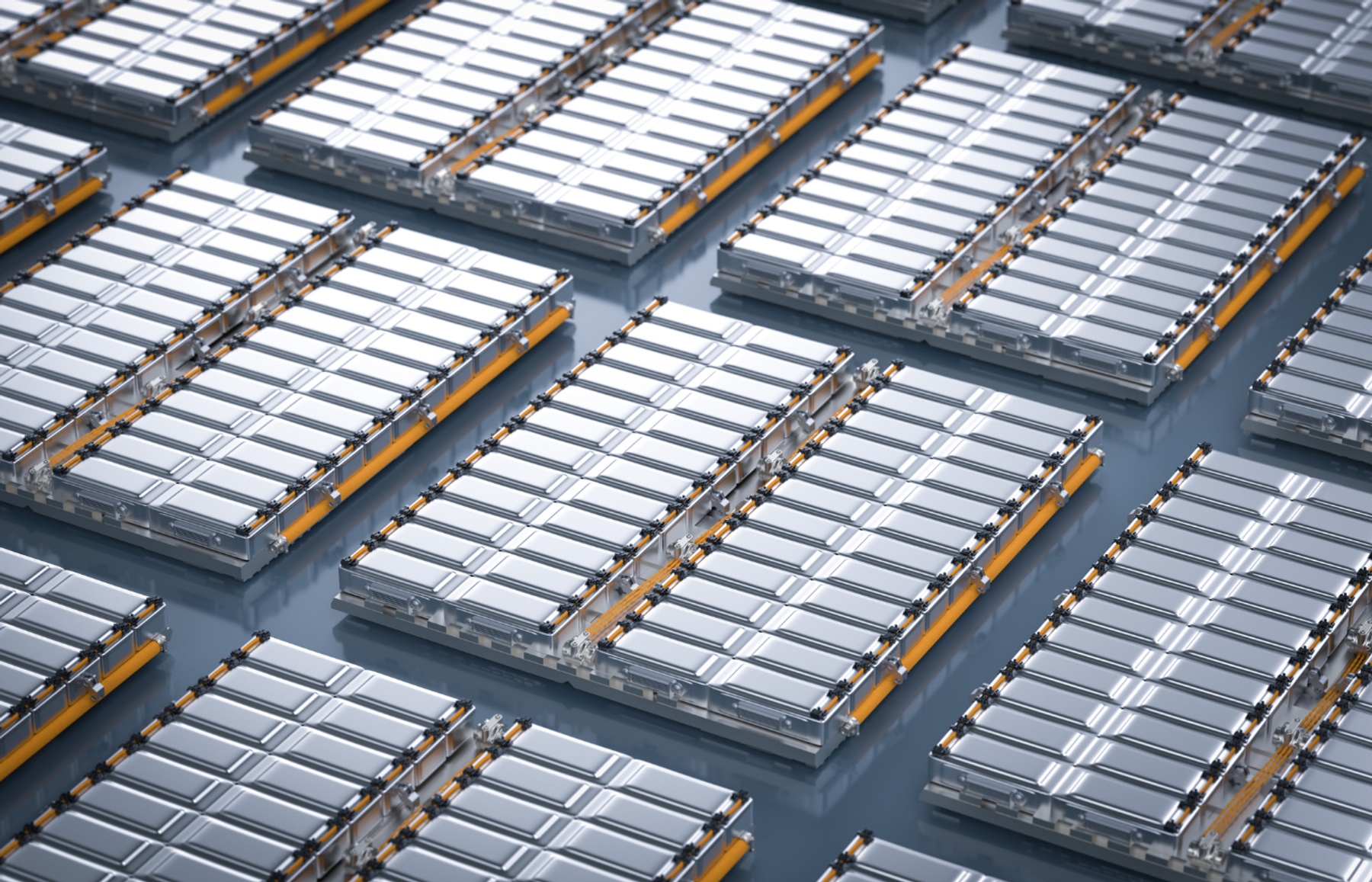 Rows of silver EV battery modules with orange connectors laid out on a grey surface