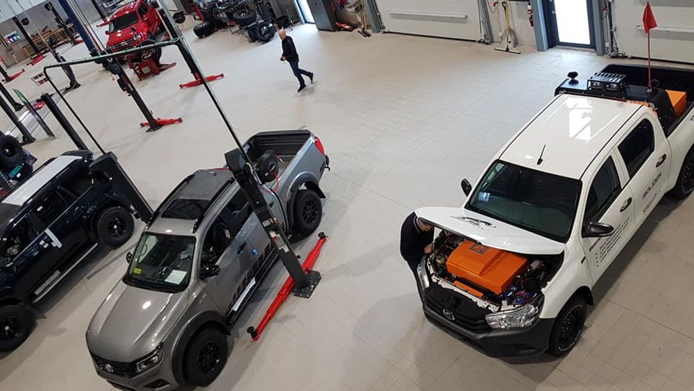 Overhead view of a workshop where a person inspects the orange electric drive unit in a white Hilux’s engine bay