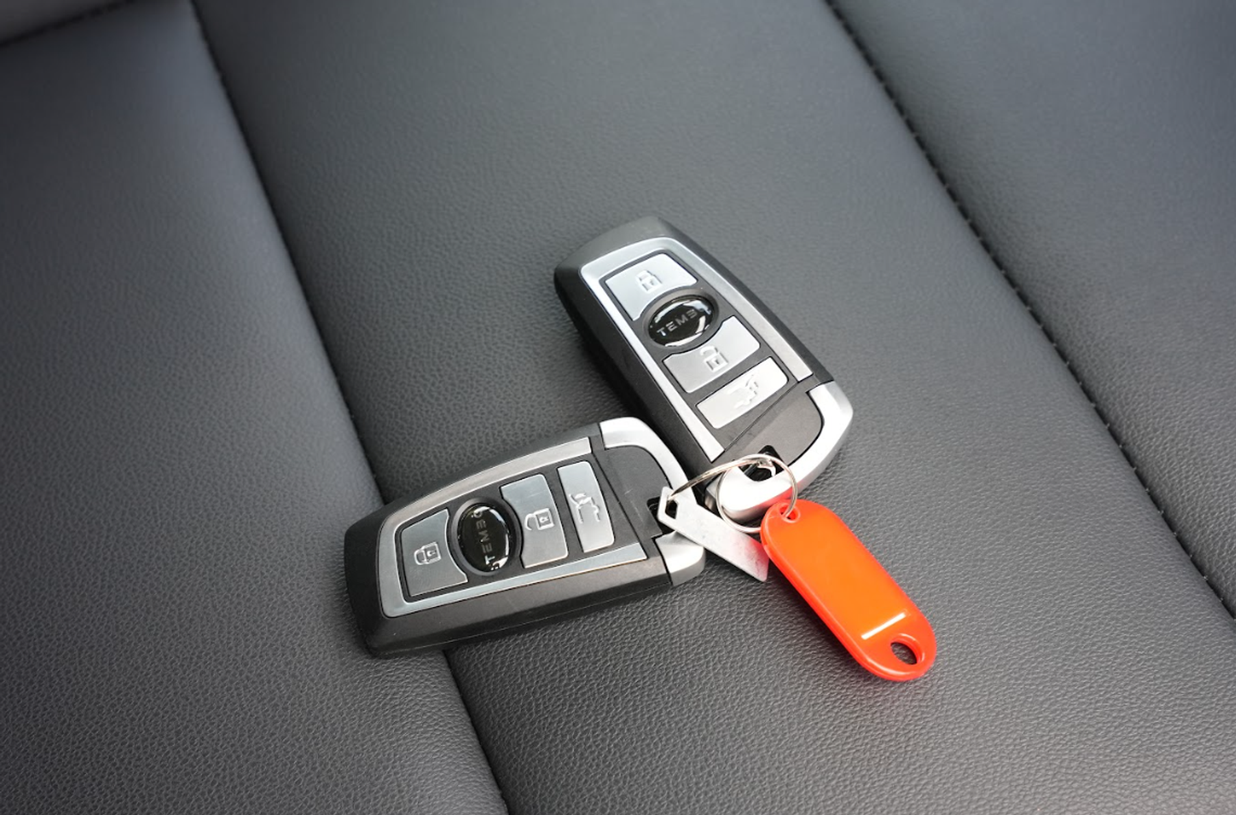 Two Tembo-branded smart keys with a red key tag resting on a black leather car seat