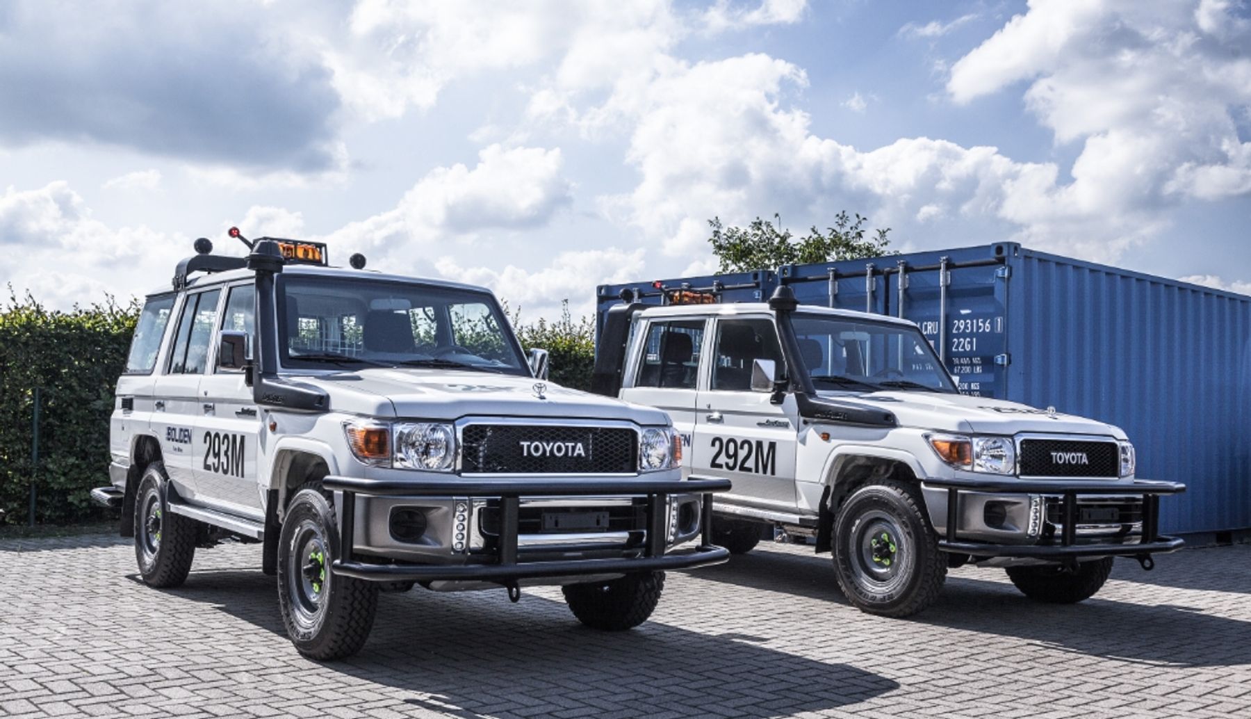 Two Boliden-branded Toyota Land Cruiser 70 series electric conversions parked by a blue shipping container