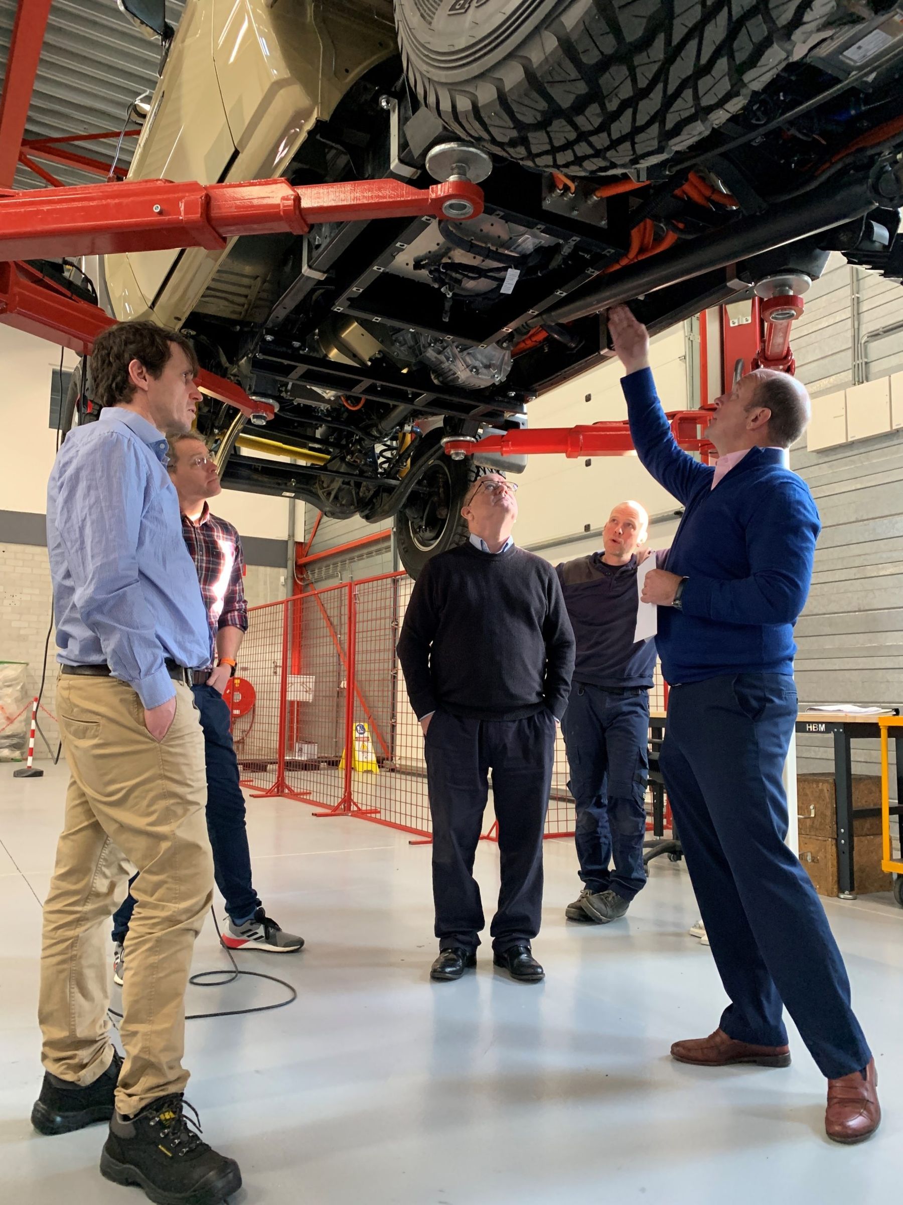 Man pointing out the electric drivetrain under a raised Land Cruiser to a group of visitors in a workshop
