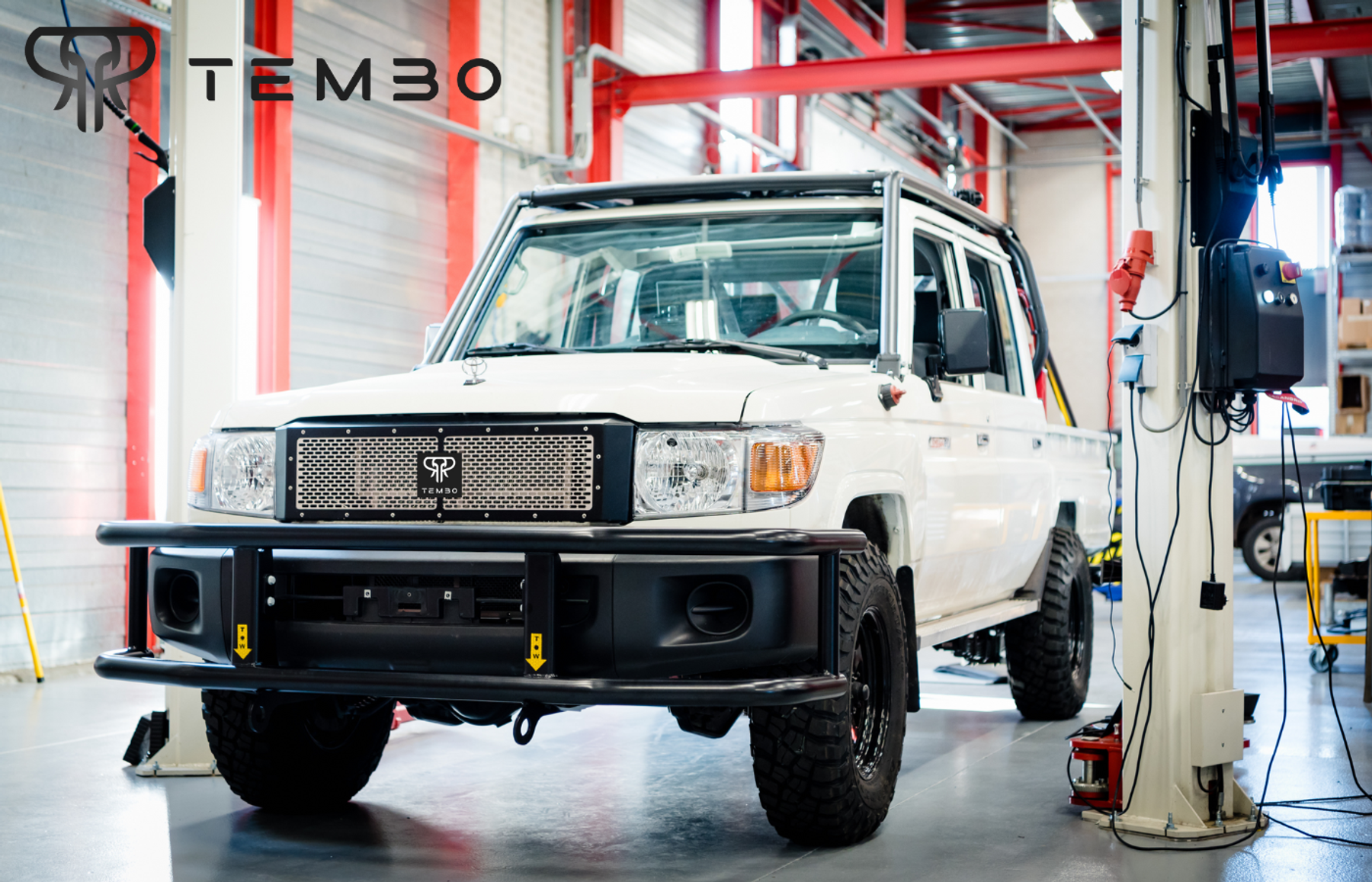 White electric Toyota Land Cruiser 70 series dual-cab with Tembo grille and bull bar in a workshop, Tembo logo