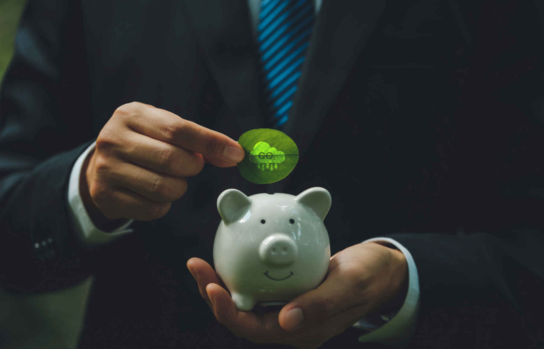 Businessman holding a piggy bank and a green leaf printed with a CO2 reduction symbol