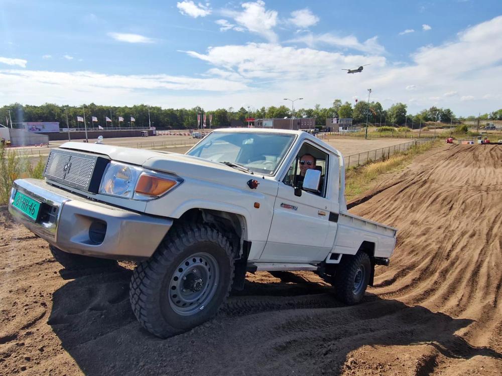 Smiling driver taking a white Tembo 4x4 e-LV single-cab Land Cruiser over a sandy motocross track during training