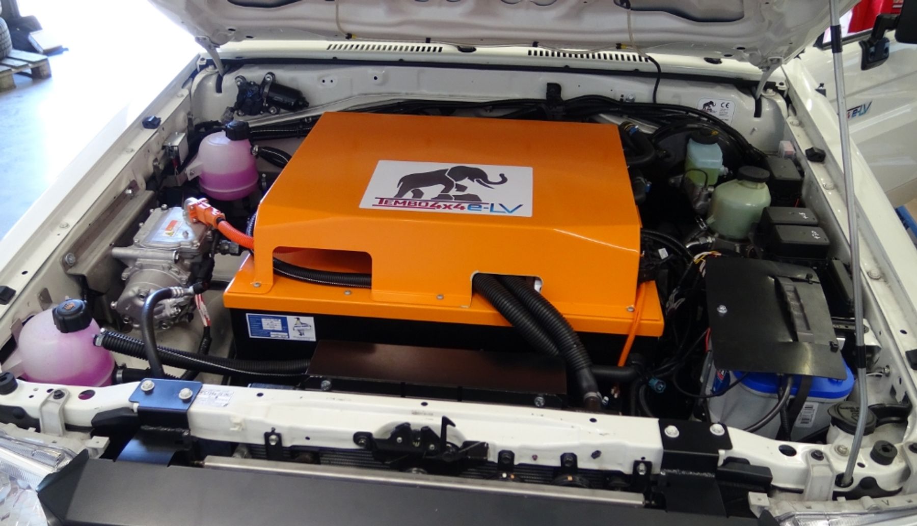 Orange Tembo 4x4 e-LV battery box fitted under the open bonnet of a converted vehicle, surrounded by cabling