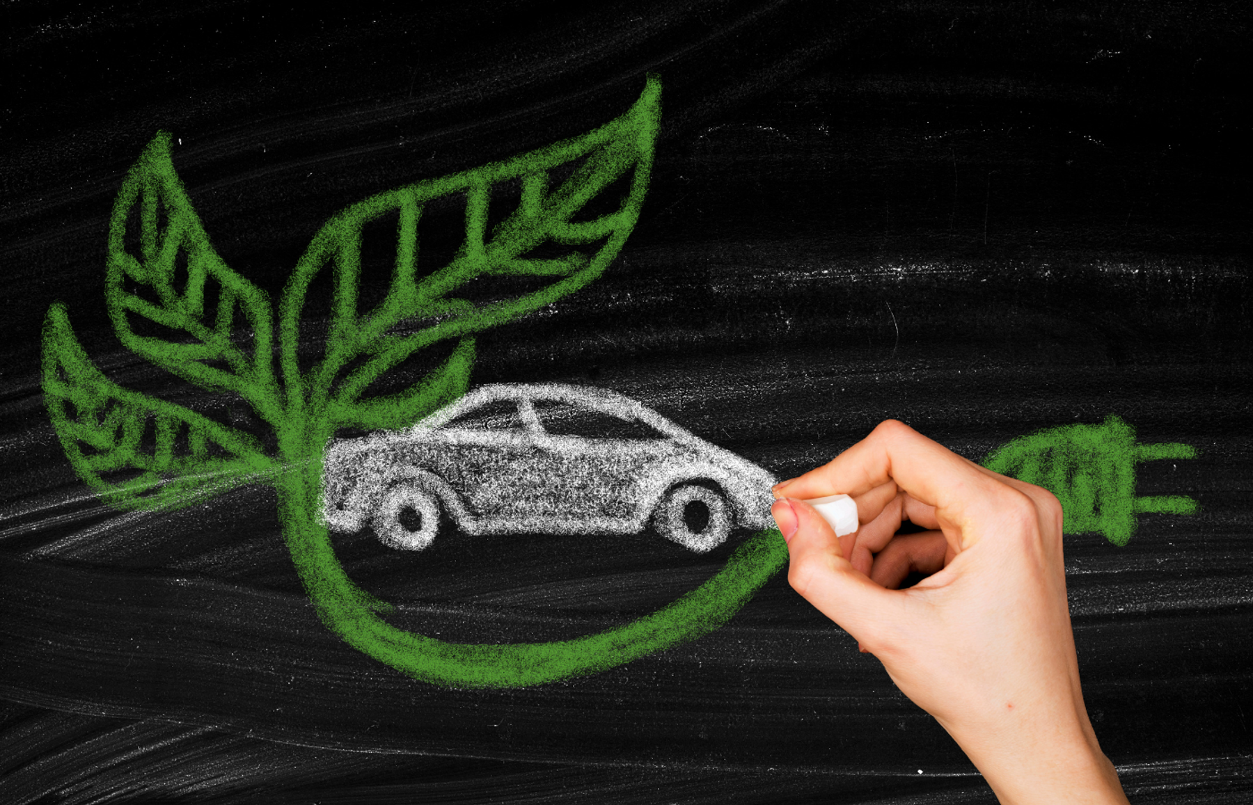 Hand drawing a car on a blackboard in white chalk, framed by green leaves and an electric plug