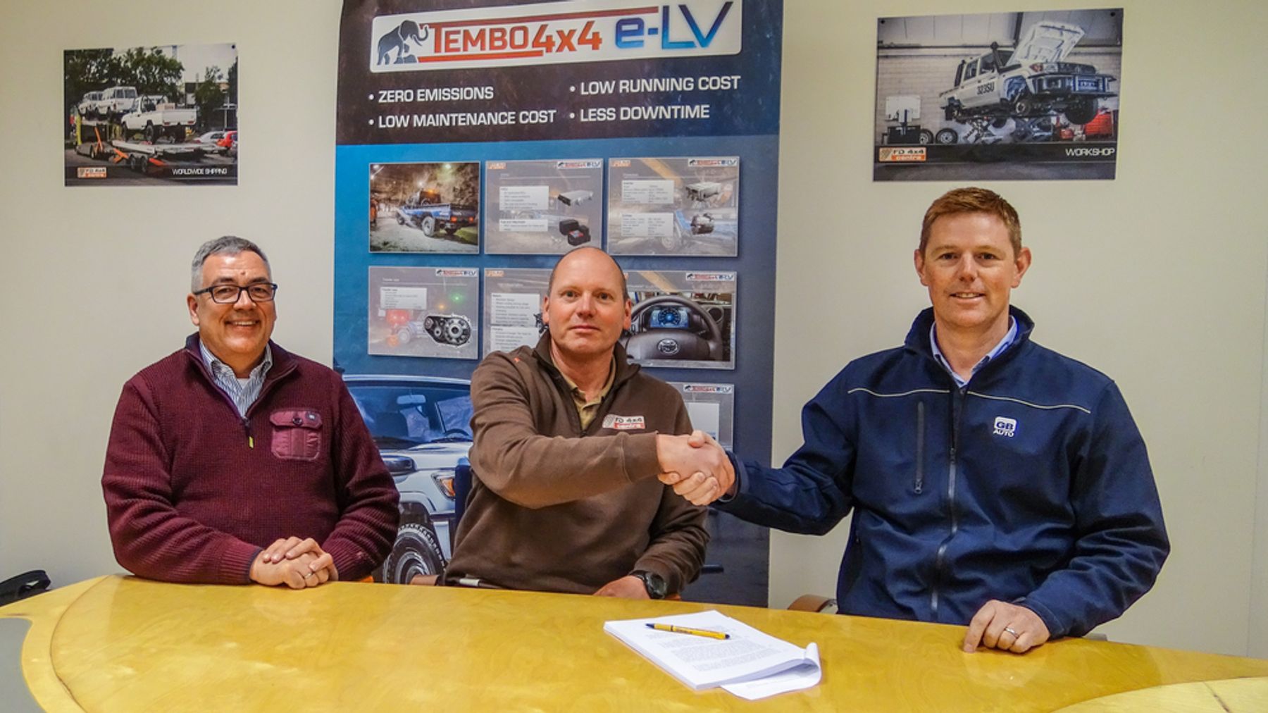 Tembo and GB Electric Vehicles representatives shaking hands over a signed agreement in front of a Tembo 4x4 e-LV banner